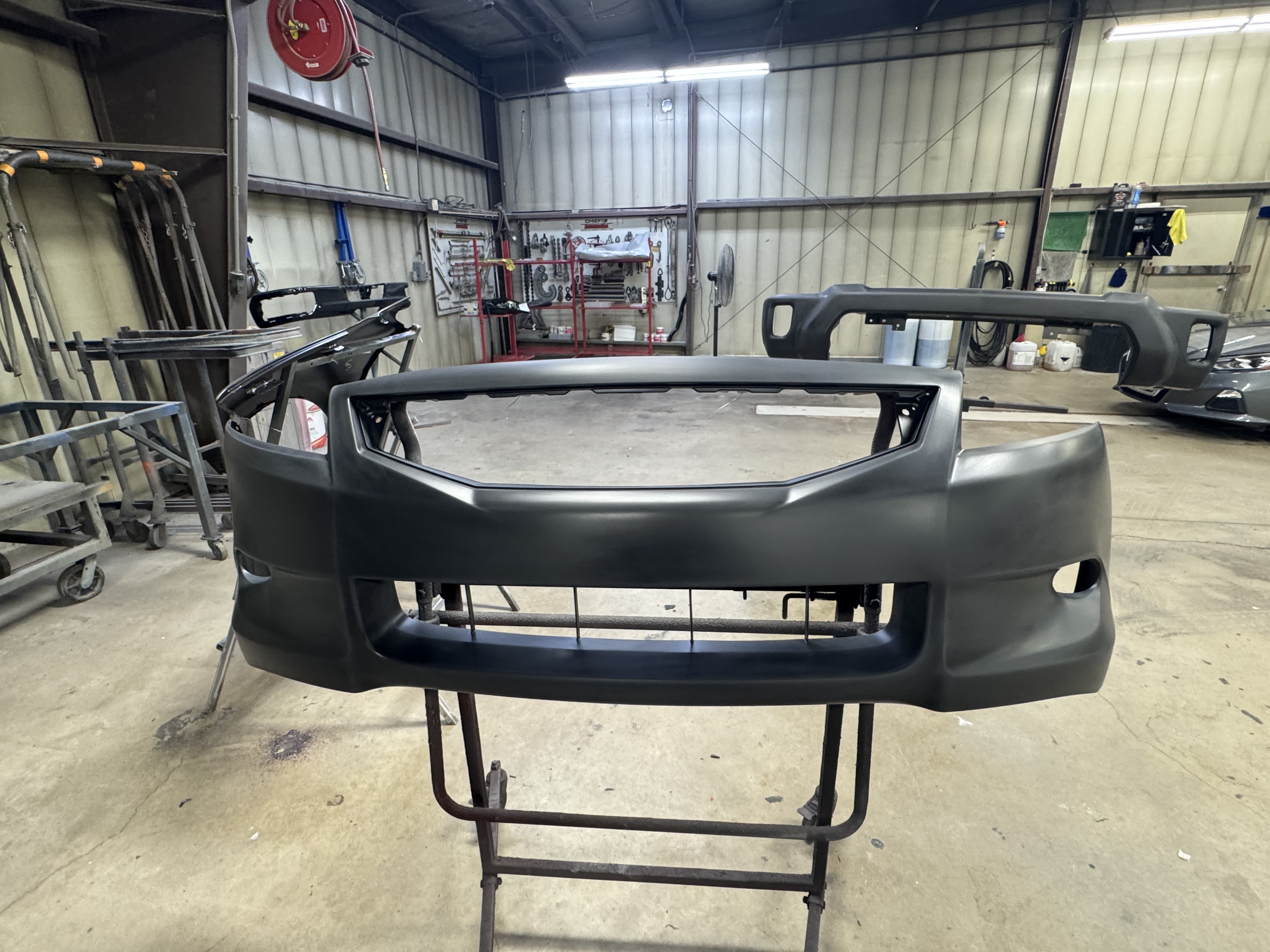 Primered front bumper cover mounted on a stand in the shop