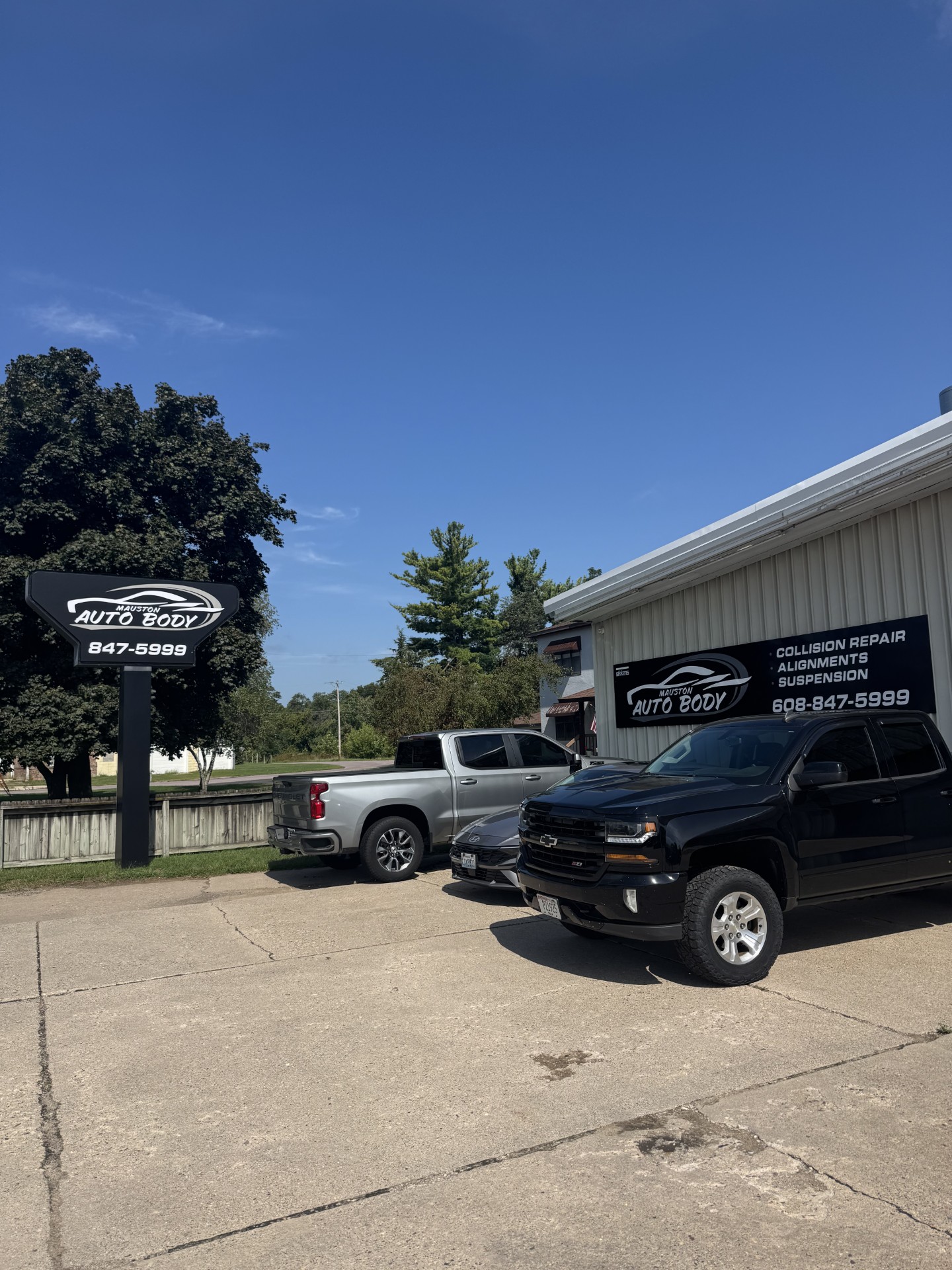Mauston Auto Body road sign and building with trucks parked outside