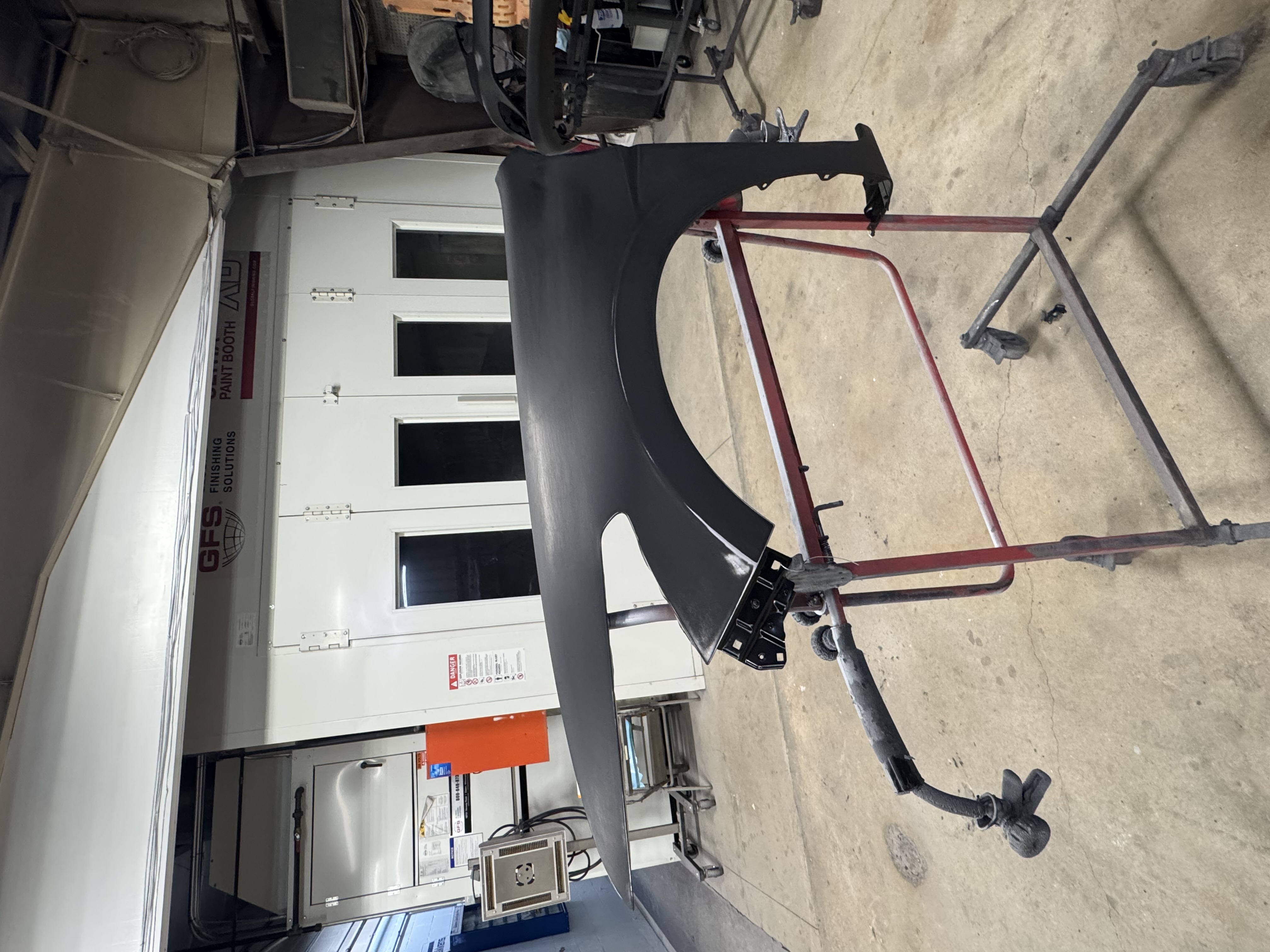 Primered fender mounted on a rolling stand in front of the paint booth