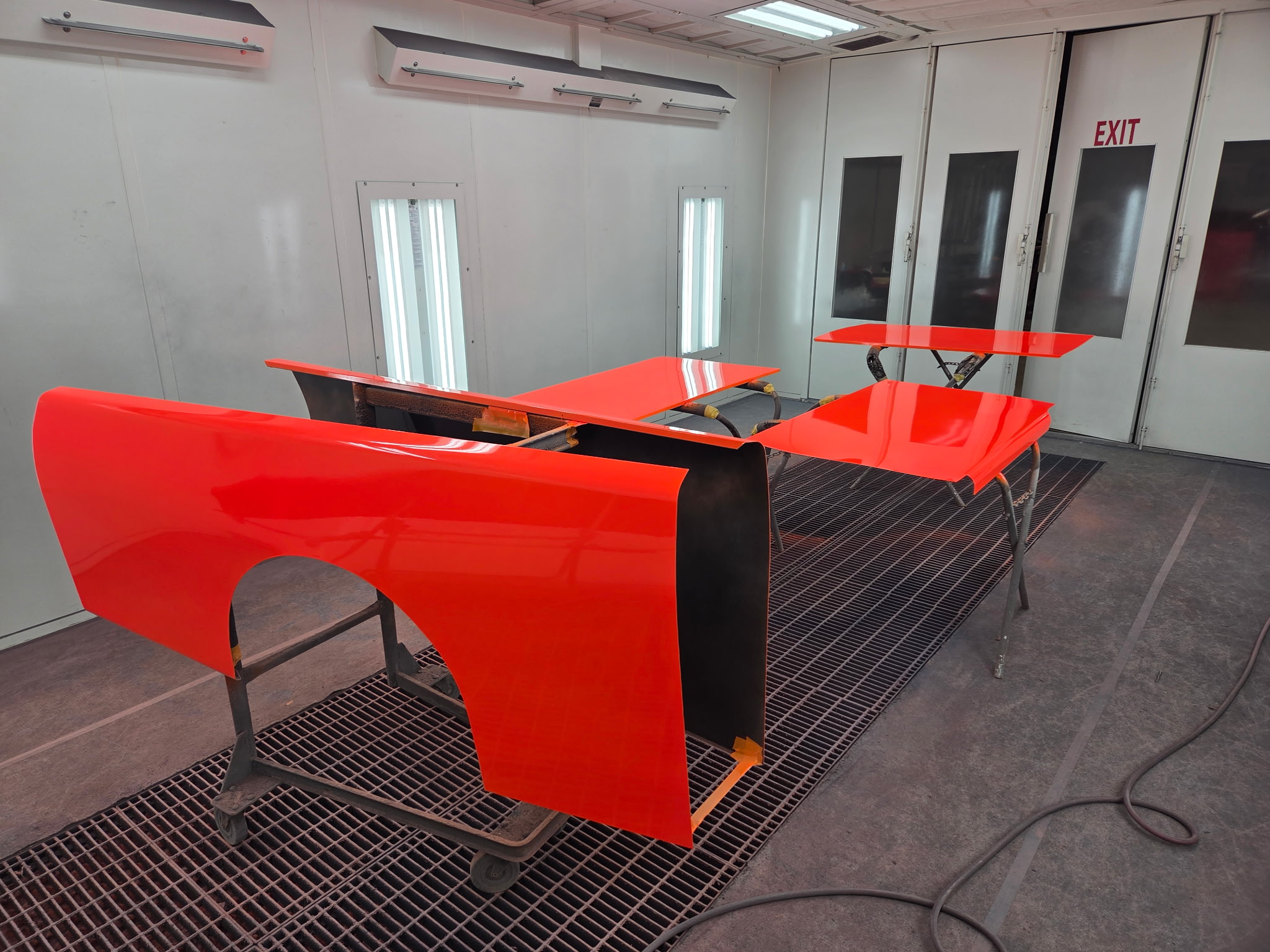Freshly painted bright orange body panels drying on stands in the booth