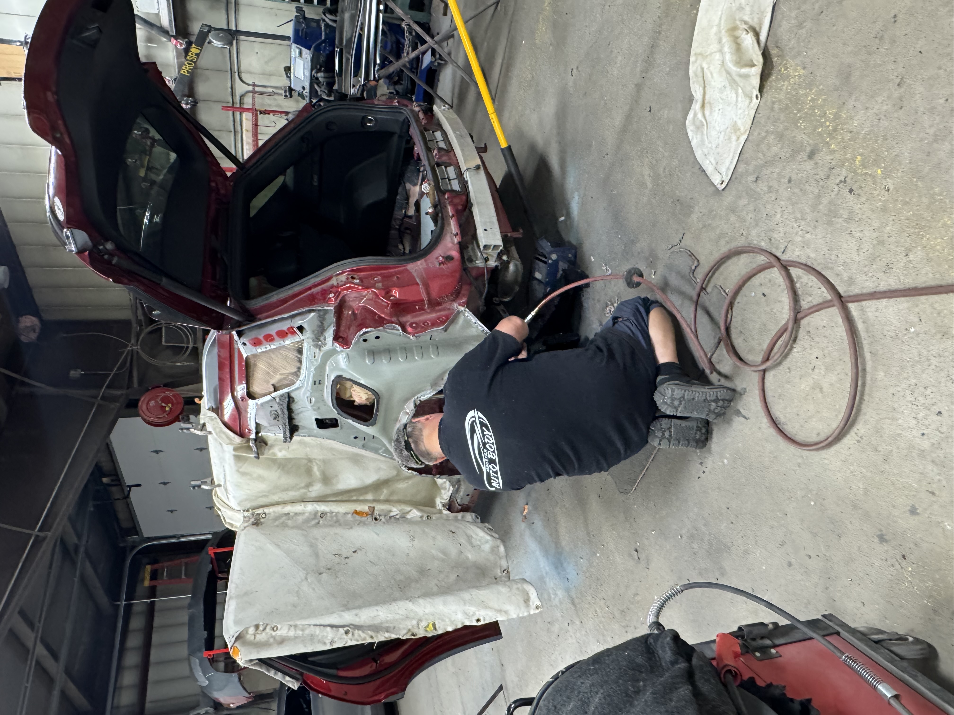 Technician performing collision repair on the rear quarter panel of a maroon SUV
