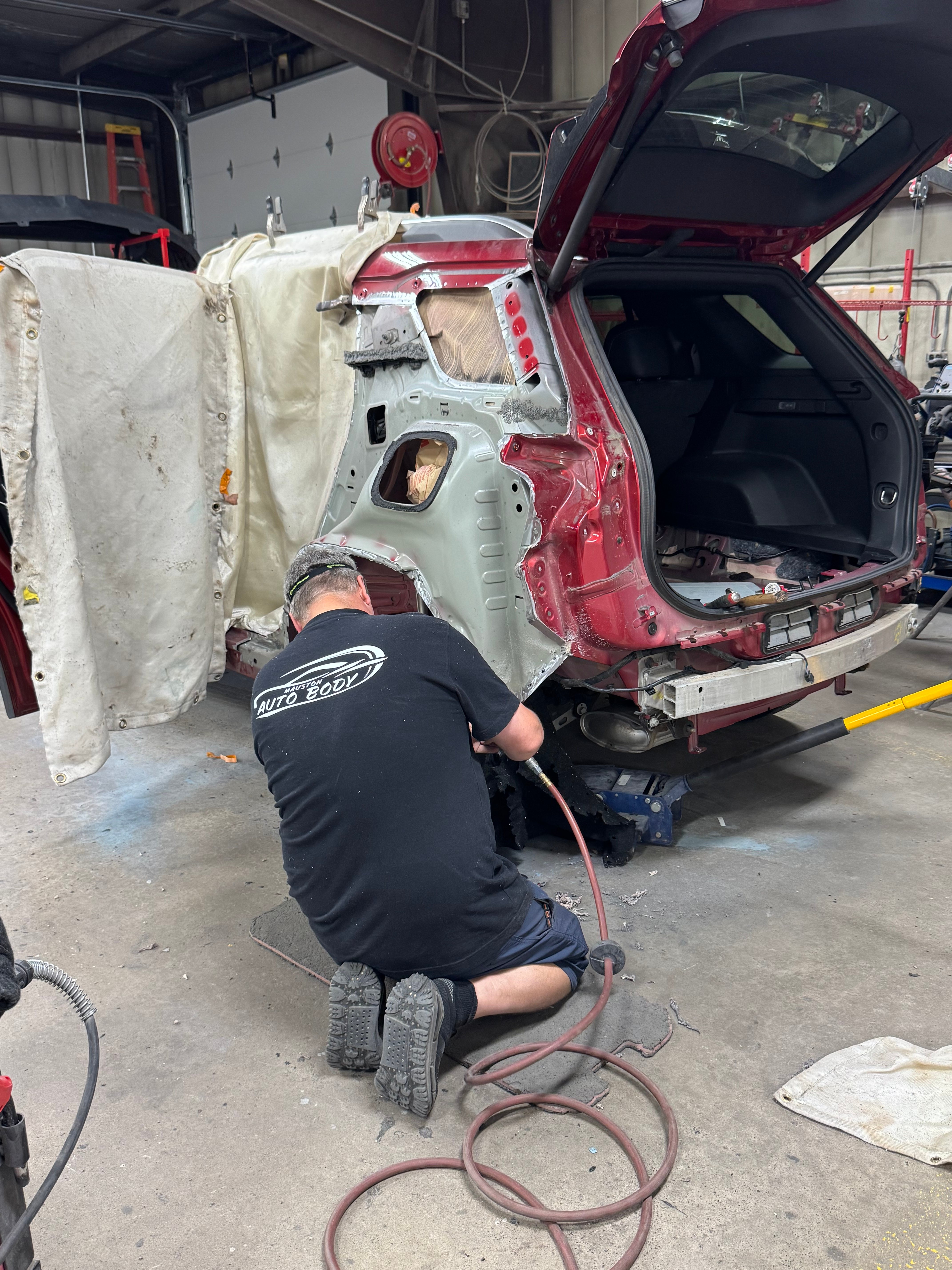 Technician working on the rear structure of a maroon SUV with the hatch open